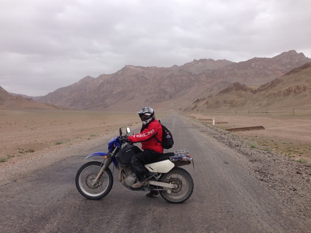 Rider standing beside a blue motorcycle in the mountains